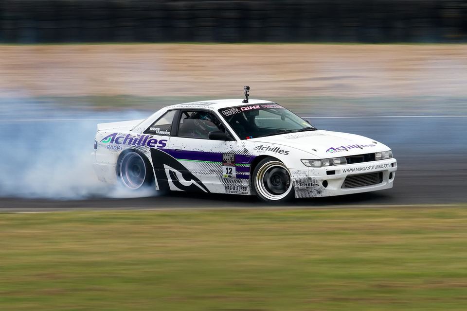 White and purple liveried drift car sliding sideways behind a wall of tyre smoke