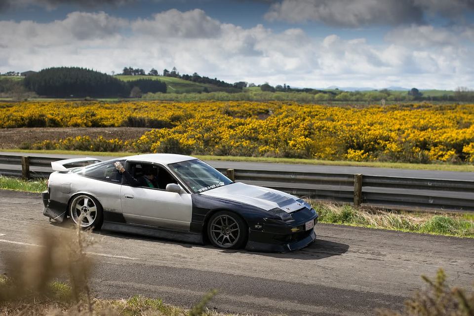 Silver coupe beside a field of yellow flowers and green hills