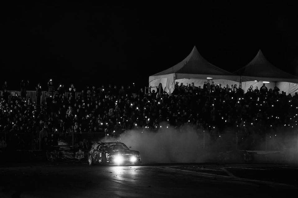 Drift car under floodlights in front of a packed night-time crowd
