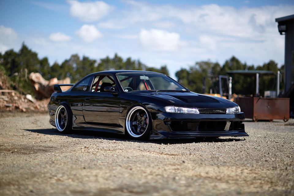 Black coupe parked on gravel under a blue sky with white clouds