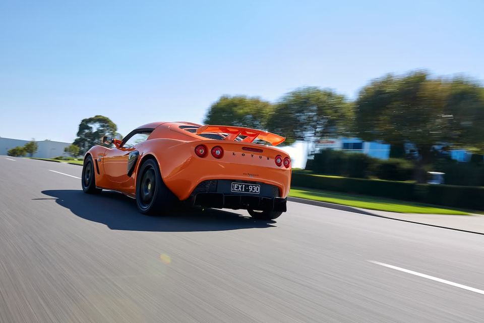 Orange sports car on an open road, wheels blurred, trees behind