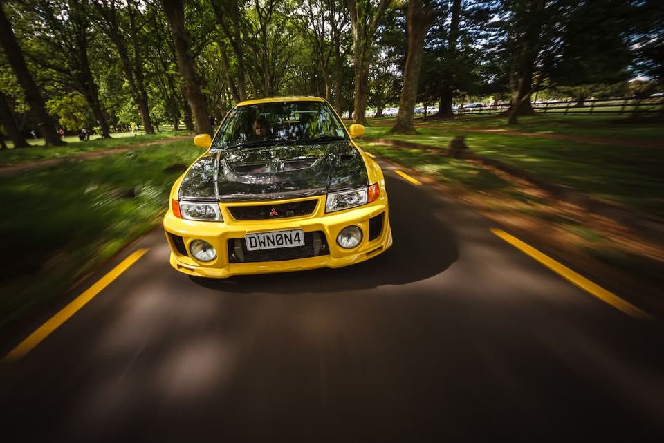 Yellow sedan on a tree-lined road in low evening light
