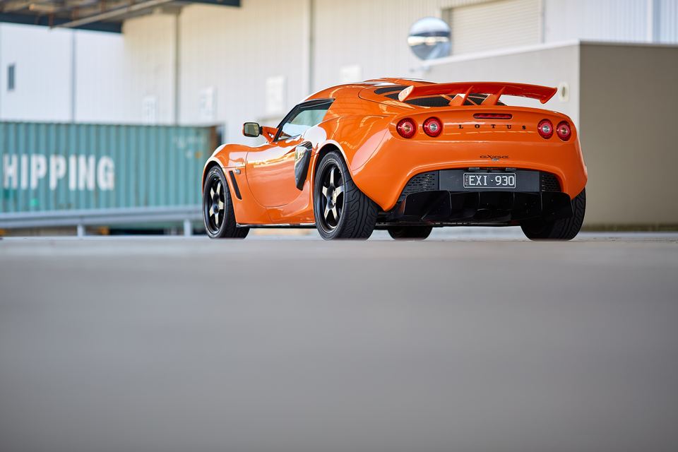 Orange sports car with a rear wing parked beside shipping containers