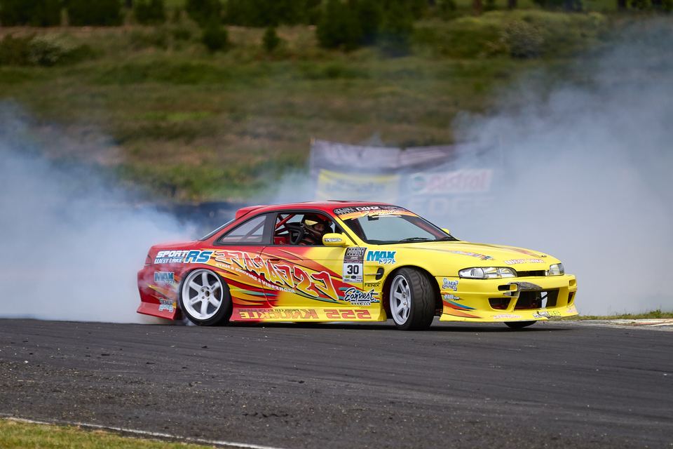 Yellow and red coupe drifting in front of a smoke cloud