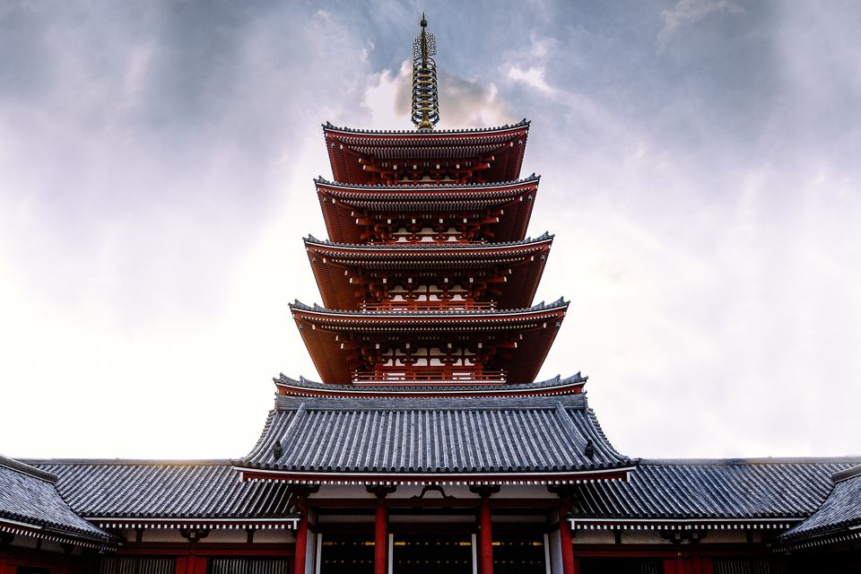 Five-storey red pagoda rising above a temple roof under a cloudy sky