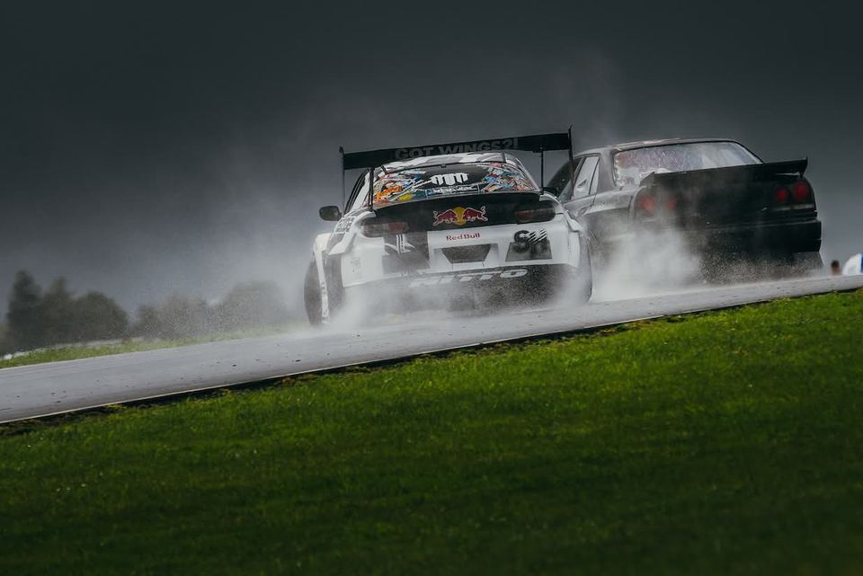 Two white cars drifting side by side through tyre smoke