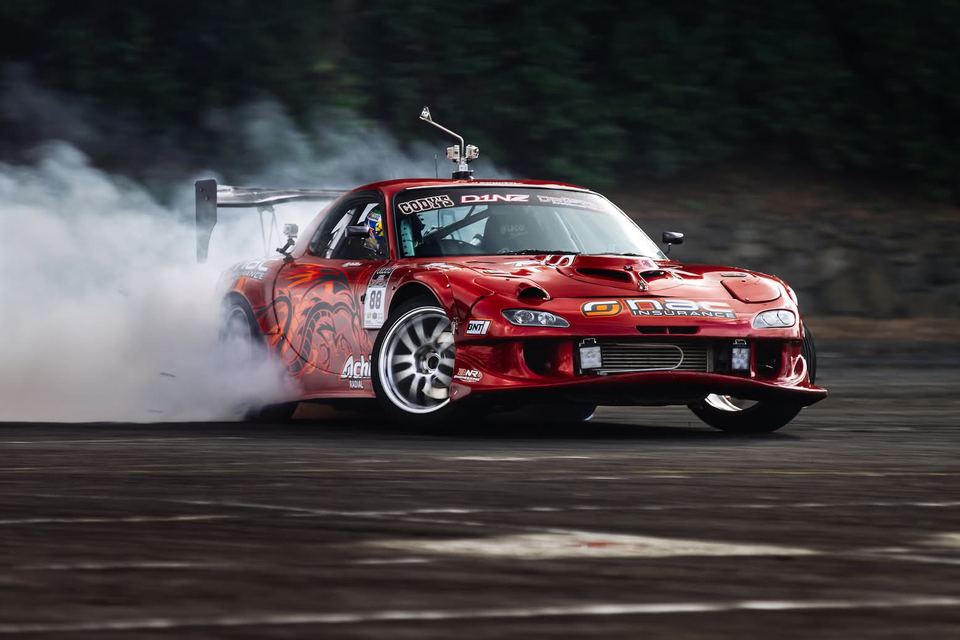 Red coupe sliding sideways with white smoke pouring off the rear tyres